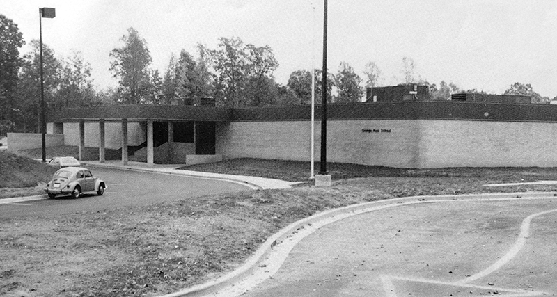 Black and white photograph from Orange Hunt's first yearbook showing the front of the building. The school grounds have been sodded, but no other plants are visible. A Volkswagen Beetle is parked in front of the school. 